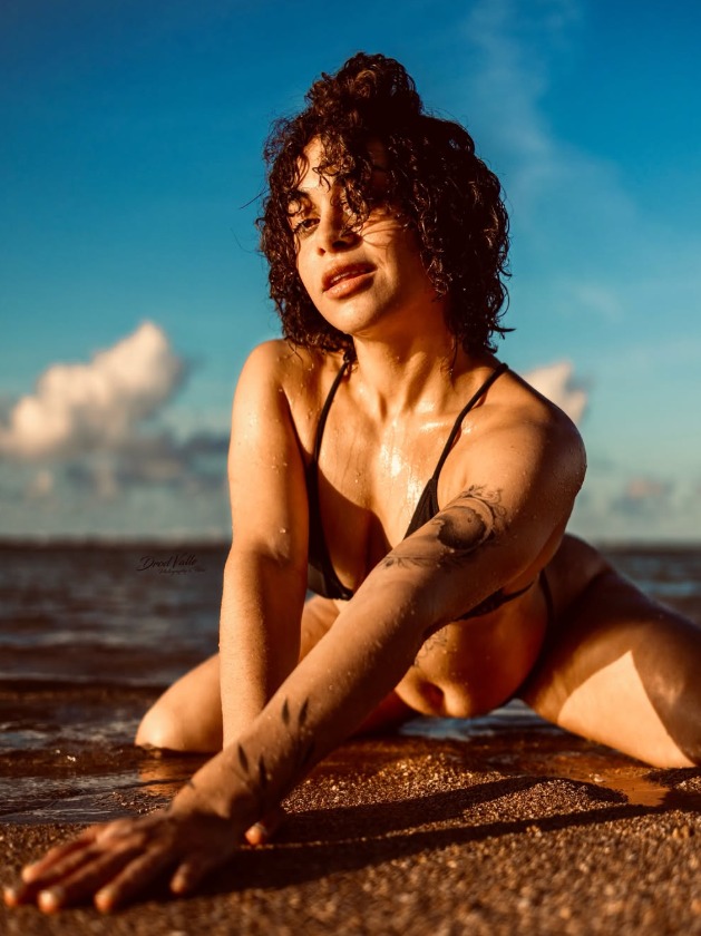 Curly Rican, a Puerto Rican OnlyFans star, in a black bikini on the beach at sunset